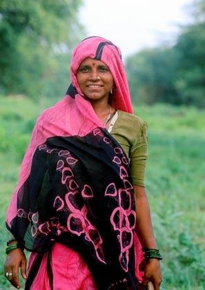 Bharatpur, Rajasthan, India: A colourfully sari-clad tribal lady cuts grass in Keoladeo Bird sanctuary.
