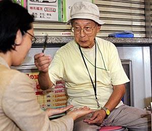 Seventy-eight-year-old fortune-teller Terutsugu Eguma attends to a customer on the street of Ginza shopping district of Tokyo.