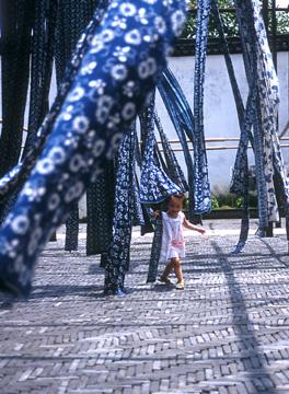 A young girl plays in the skeins of traditional blue and white tie-died fabric as they dry in a courtyard.