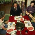 These guests are seated around a dinner table featuring one of Japan's many 'hot pot' dishes. Diners cook their own food in the simmering broth and remove it one bite at at time.