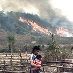 A young woman with a baby in the fields as vegetation is burnt off in the background, at a Hmong village resettled in the Xiengkhone district of the northern Laos province of Xayaburi.